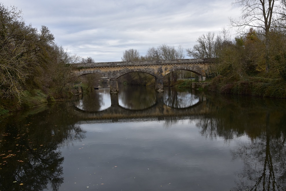 Pont ferroviaire en pierre à trois arches se reflétant dans une rivière, sur l'ancienne ligne de La Possonnière à Niort